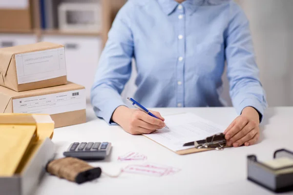 Femme avec presse-papiers et colis au bureau de poste — Photo