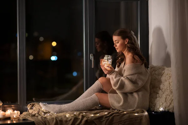 Frau mit Lichtergirlanden im Glasbecher zu Hause — Stockfoto