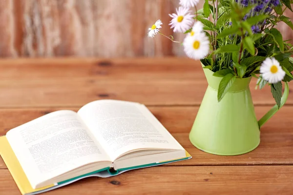 Libro y flores en jarra sobre mesa de madera — Foto de Stock