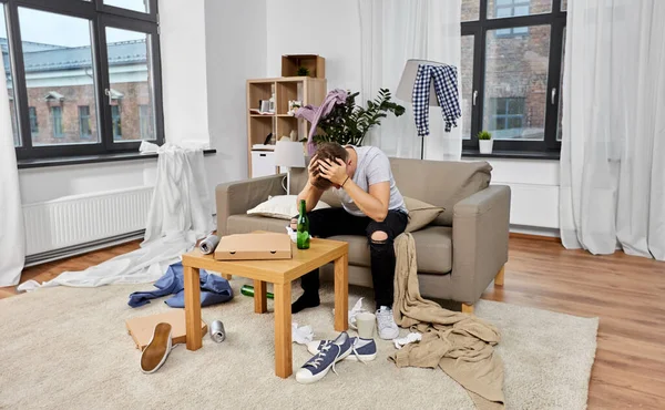 Drunk man sitting on sofa in messy room at home — Stock Fotó