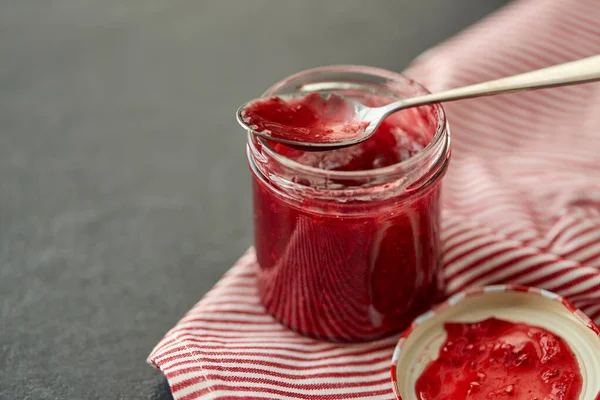 Murer krukke med hindbær marmelade og ske på håndklæde - Stock-foto