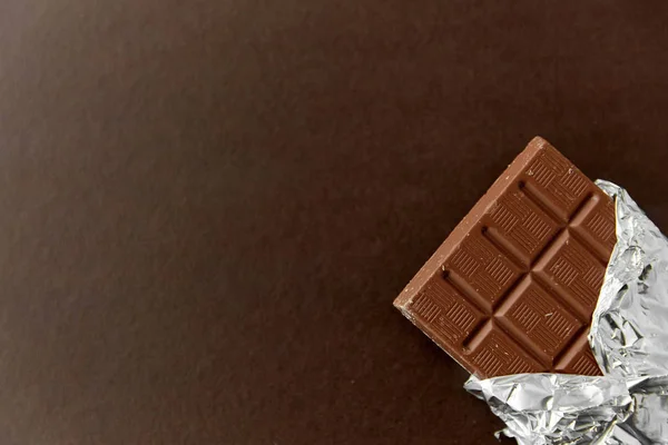 Chocolate bar in foil wrapper on brown background — Stock Photo, Image