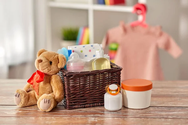 Baby things in basket and teddy bear toy on table — 图库照片