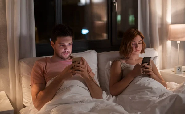 Coppia utilizzando smartphone a letto di notte a casa — Foto Stock