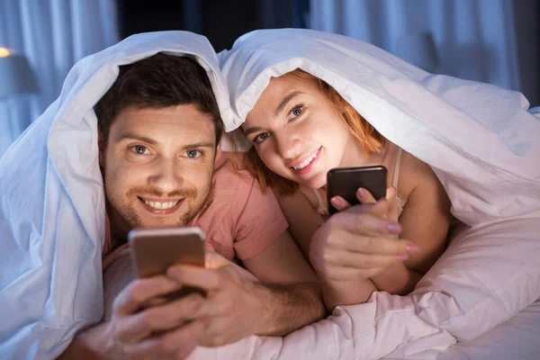 Glückliches Paar nutzt Smartphone nachts im Bett — Stockfoto