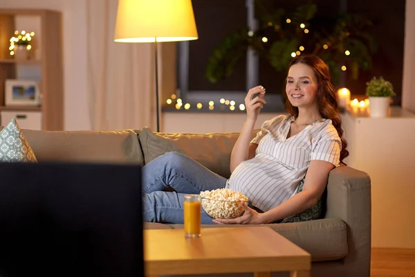 Pregnant woman with popcorn watching tv at home Royaltyfria Stockbilder