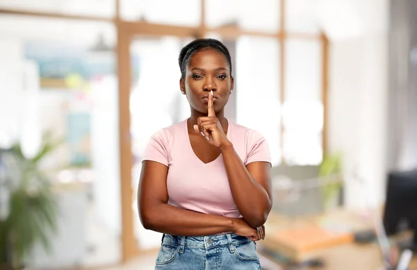 Mujer africana con el dedo en los labios en la oficina — Foto de Stock