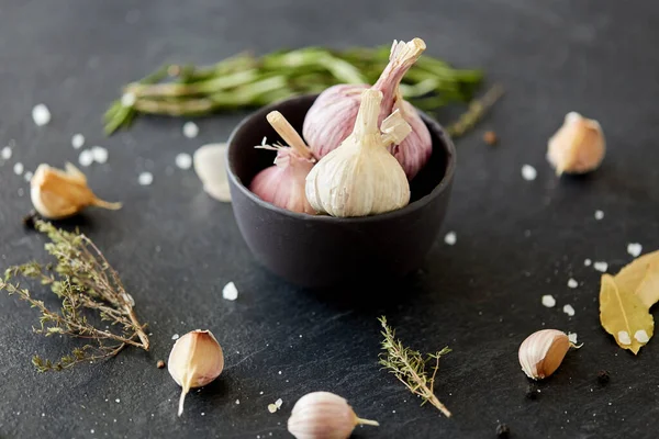 Garlic in bowl and rosemary on stone surface — Zdjęcie stockowe