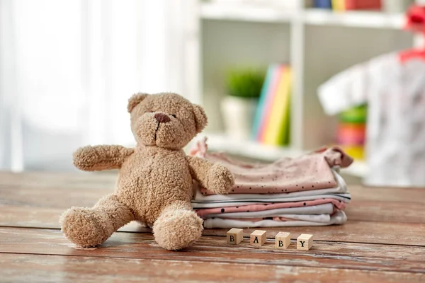 Baby clothes and teddy bear toy on table at home — Stock Photo, Image