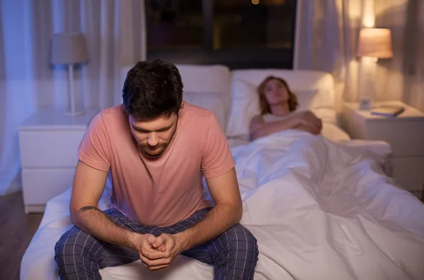 Sad man with insomnia sitting on bed at night — Stockfoto