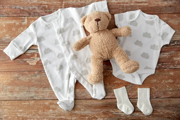 Bebek kıyafetleri ve oyuncak ayı ahşap masada Telifsiz Stok Fotoğraflar