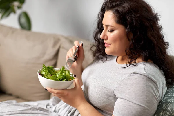 Sonriente mujer joven comiendo ensalada de verduras en casa — Foto de Stock