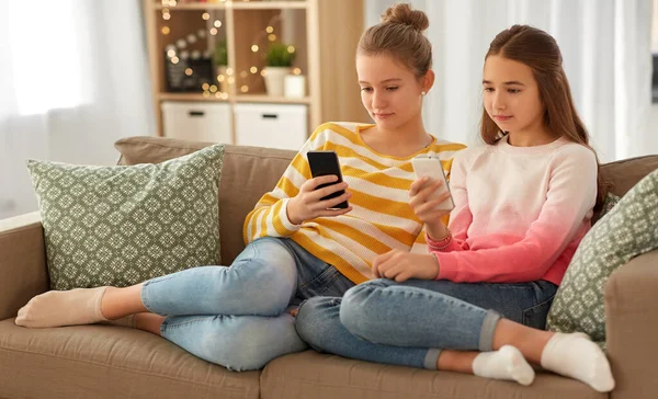 Meninas com smartphones sentados no sofá em casa — Fotografia de Stock