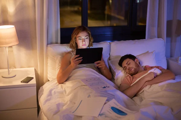 Женщина с планшетным компьютером работает в постели ночью — стоковое фото