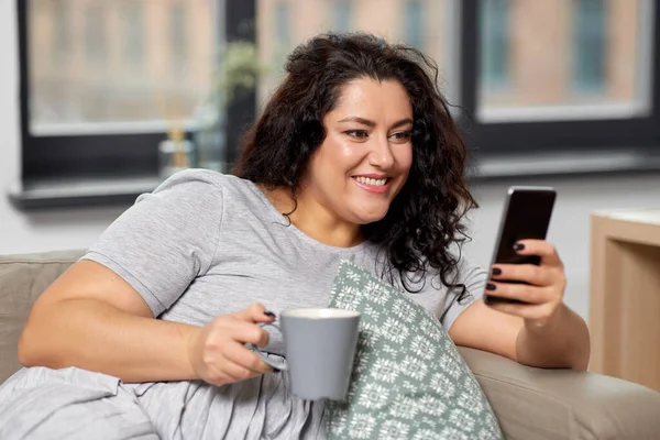 Žena s chytrým telefonem pití kávy doma — Stock fotografie