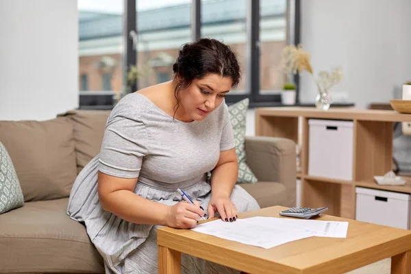 Kobieta z rachunkami lub papierami i kalkulatorem w domu — Zdjęcie stockowe