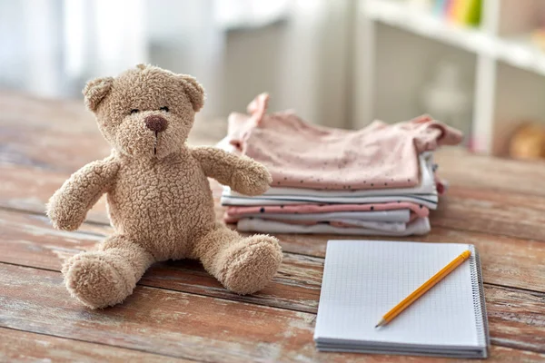 Baby clothes, teddy bear toy and notebook — Stock Photo, Image