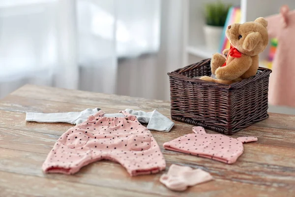 Ropa de bebé y juguete de oso de peluche en la cesta en casa —  Fotos de Stock