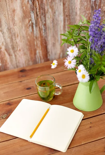 Chá de ervas, caderno e flores em jarro na mesa — Fotografia de Stock