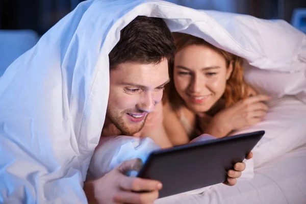 Happy couple using tablet pc in bed at night — Stock Photo, Image