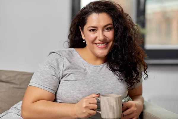 Mutlu kadın evdeki kanepede çay ya da kahve içiyor. — Stok fotoğraf