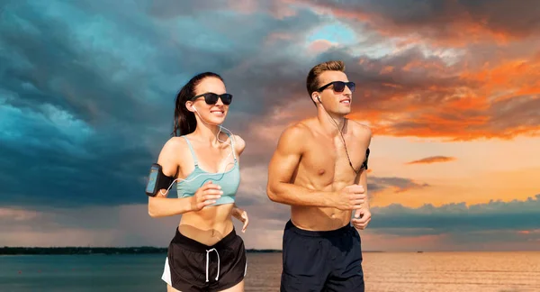 Couple with phones and arm bands running over sea — Stock Photo, Image