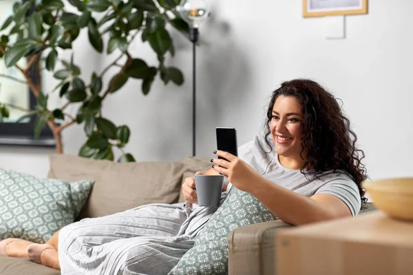 Kvinna med smartphone dricka kaffe hemma — Stockfoto