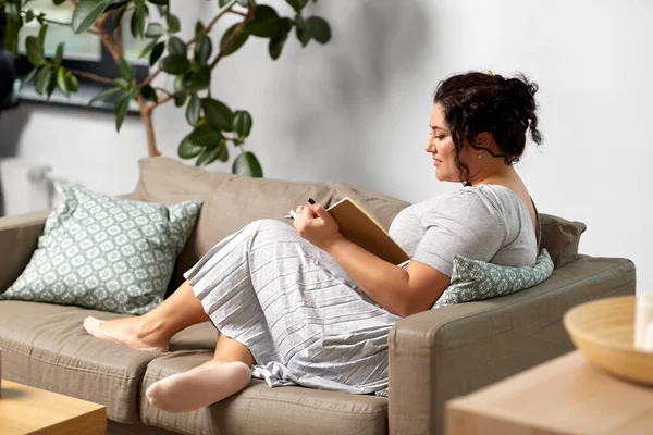 Šťastná mladá žena s deníkem na pohovce doma — Stock fotografie