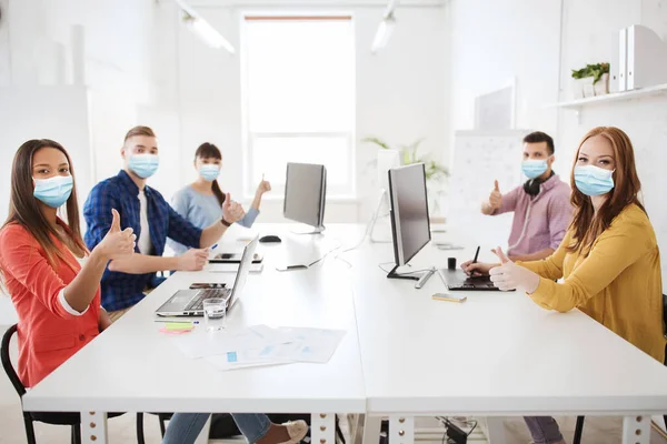 Business team in medical masks showing thumbs up — Stock fotografie