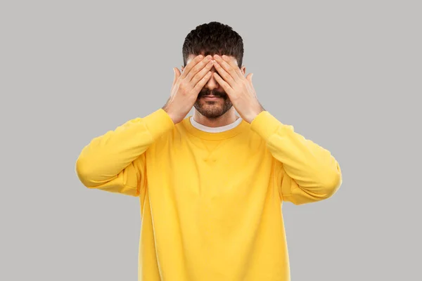 Man in yellow sweatshirt closing his eyes by hands — Zdjęcie stockowe