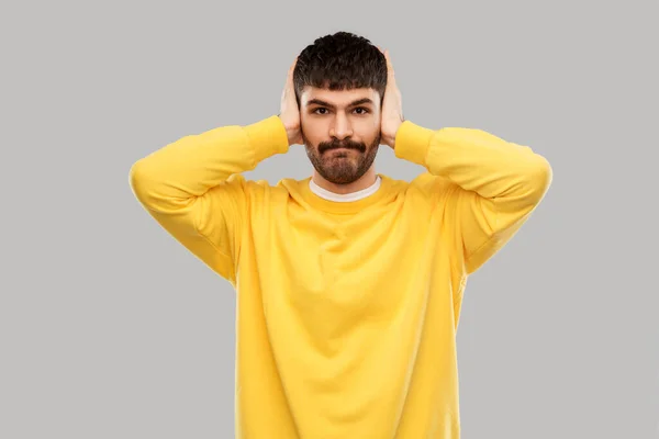 Man in yellow sweatshirt closing ears by hands — Zdjęcie stockowe