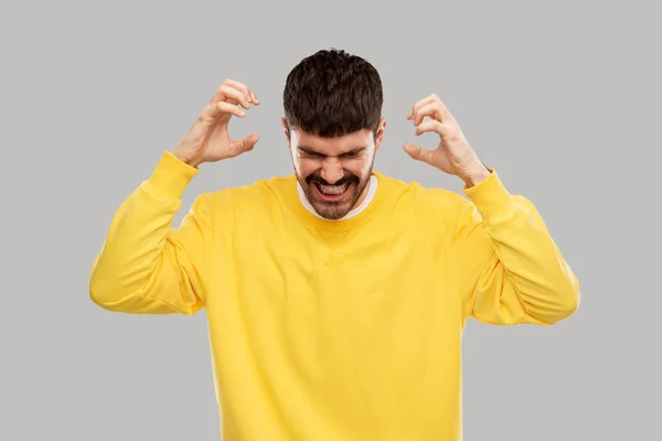 Angry young man in yellow sweatshirt over grey — 图库照片