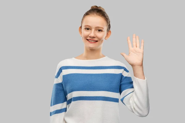 Улыбающаяся девушка-подросток в пуловере машет рукой — стоковое фото