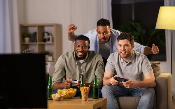 Amigos felices jugando videojuegos en casa por la noche — Foto de Stock