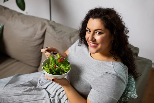 Gülümseyen genç kadın evde sebze salatası yiyor. — Stok fotoğraf