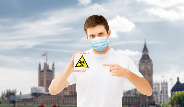 Hombre con máscara médica con signo de peligro biológico en Inglaterra —  Fotos de Stock
