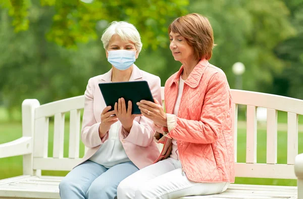 Starsze kobiety w masce medycznej z tabletem w parku — Zdjęcie stockowe