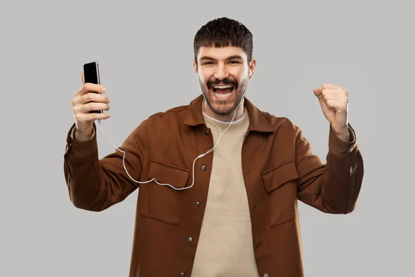 Χαμογελαστός νεαρός άνδρας με ακουστικά και smartphone — Φωτογραφία Αρχείου