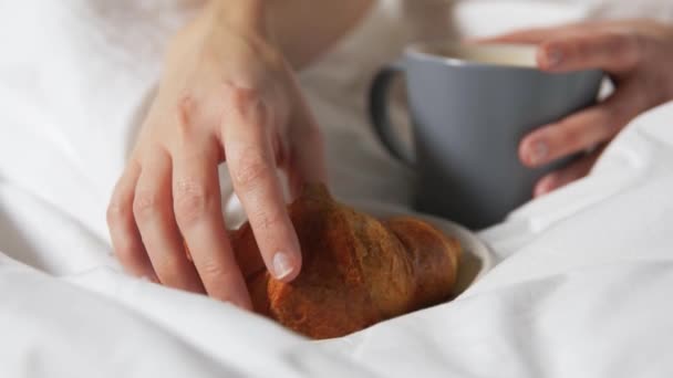 Hand of woman eating croissant with coffee in bed — Stock Video