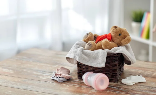 Игрушка плюшевого мишки в корзине с детскими вещами на столе — стоковое фото