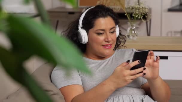 ヘッドフォンの女性はスマートフォンで音楽を聴き — ストック動画