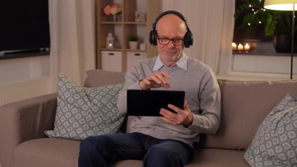 Äldre man med TabletPC och hörlurar hemma — Stockvideo