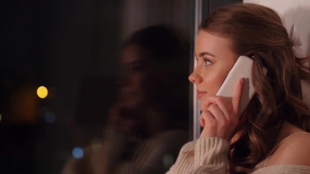 Mujer joven llamando en el teléfono inteligente en la ventana — Vídeos de Stock