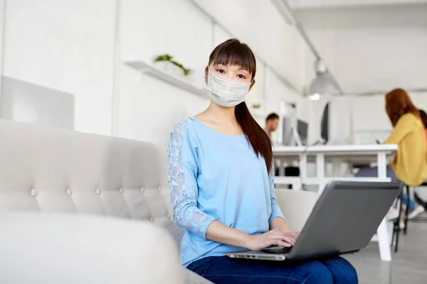 Asiatin mit Laptop in Arztmaske im Büro — Stockfoto
