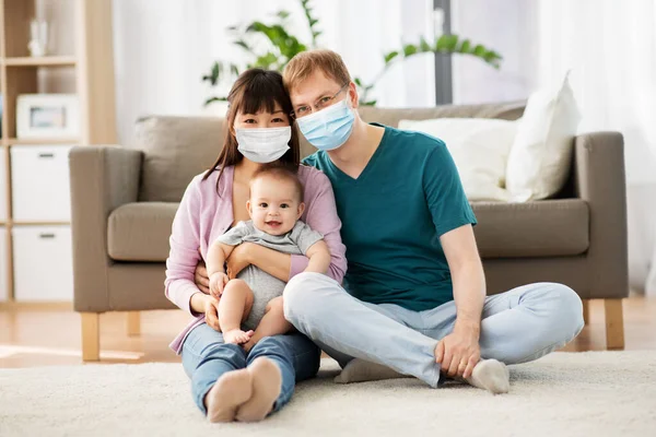 family with baby in medical masks at home