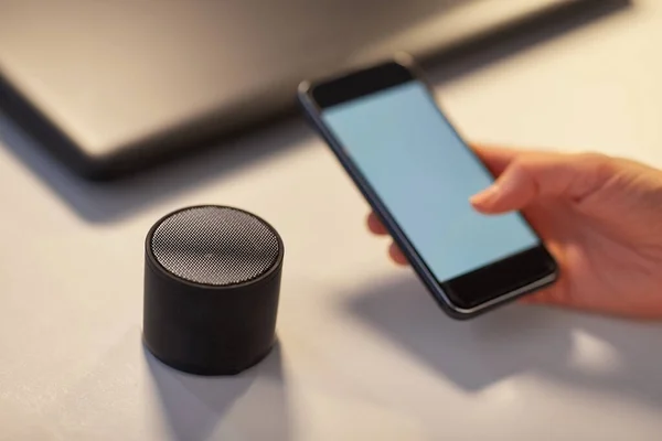 Hand with smartphone and smart speaker at office — Stock Photo, Image