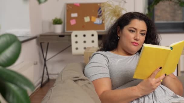 Junge Frau liest Buch zu Hause auf dem Sofa — Stockvideo