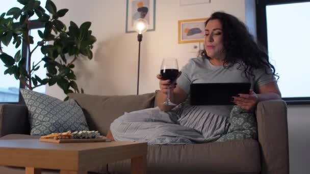 Frau mit Tablet-PC trinkt zu Hause Rotwein — Stockvideo