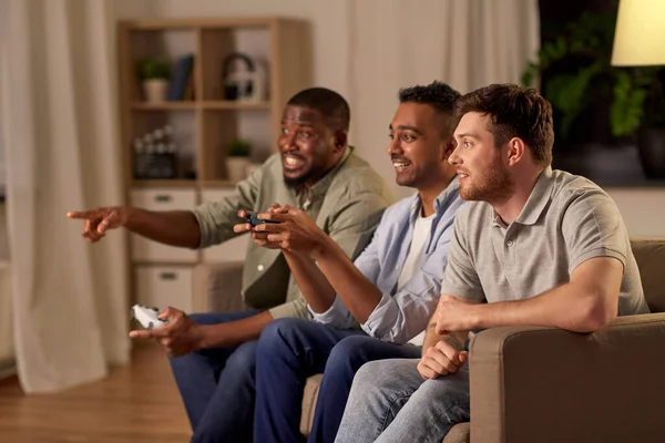 Amigos felices jugando videojuegos en casa por la noche —  Fotos de Stock