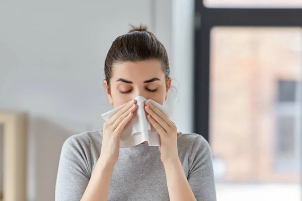 Sick woman blowing nose in paper tissue at home — Stock Photo, Image